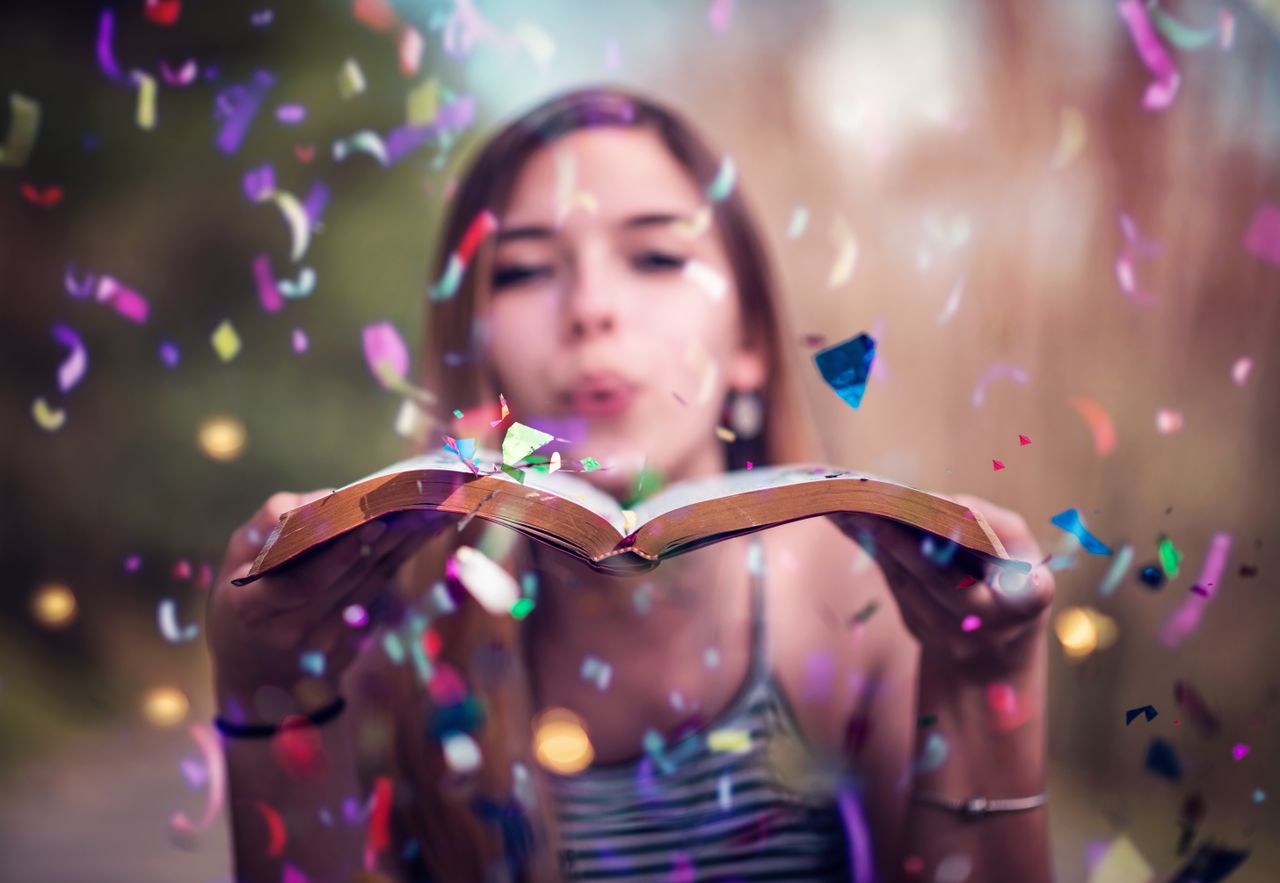 Cette image montre une jeune femme qui souffle des confettis sur un livre ouvert